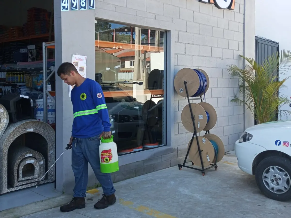 Técnico da DDKA com pulverizador na calçada de um comércio